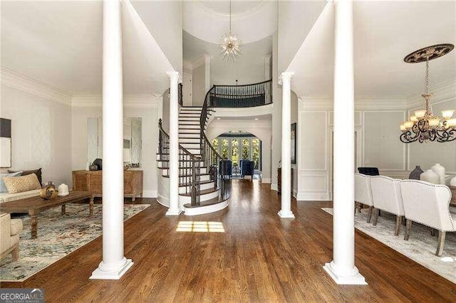 entryway with dark wood-type flooring, ornate columns, a notable chandelier, and ornamental molding