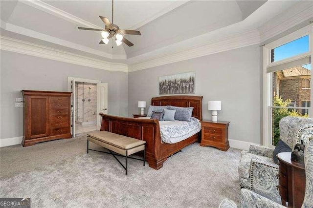 carpeted bedroom with a tray ceiling, ornamental molding, connected bathroom, and ceiling fan