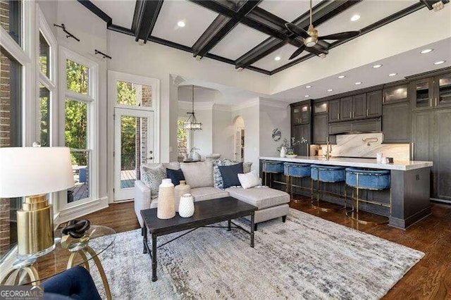 living room with crown molding, dark hardwood / wood-style flooring, coffered ceiling, ceiling fan, and beam ceiling