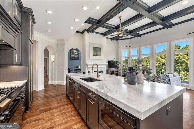 kitchen featuring coffered ceiling, hardwood / wood-style floors, beam ceiling, an island with sink, and sink