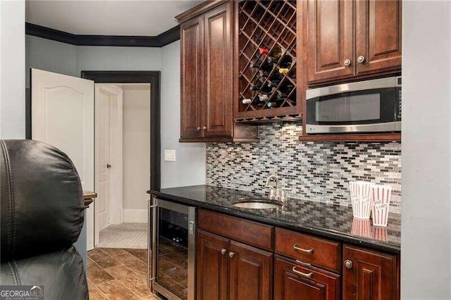 kitchen featuring wine cooler, backsplash, ornamental molding, sink, and dark stone countertops