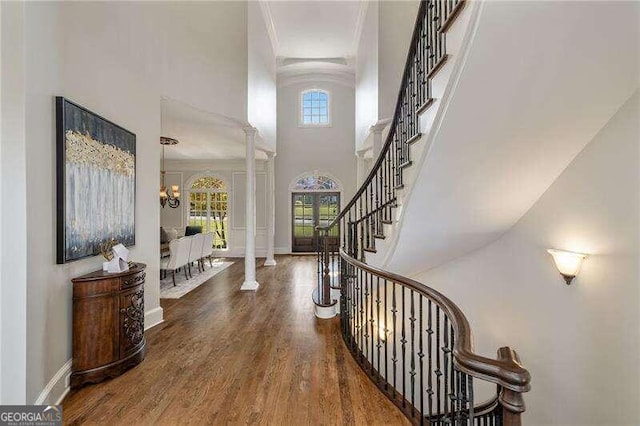 entrance foyer featuring crown molding, hardwood / wood-style flooring, ornate columns, and an inviting chandelier