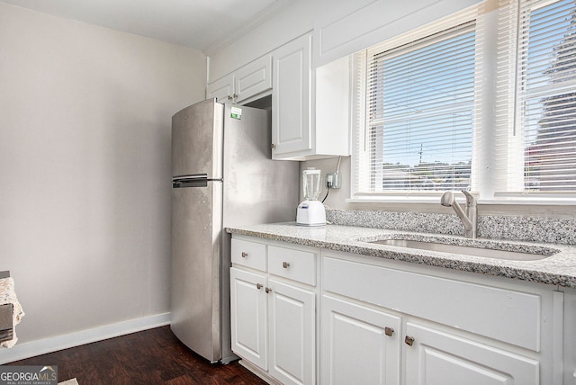 kitchen featuring light stone countertops, dark hardwood / wood-style floors, white cabinets, stainless steel fridge, and sink