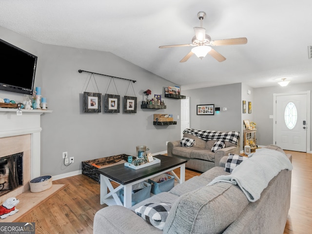 living room with wood-type flooring, ceiling fan, a fireplace, and vaulted ceiling