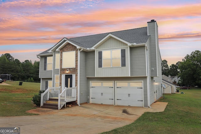 raised ranch featuring a lawn, driveway, roof with shingles, an attached garage, and a chimney