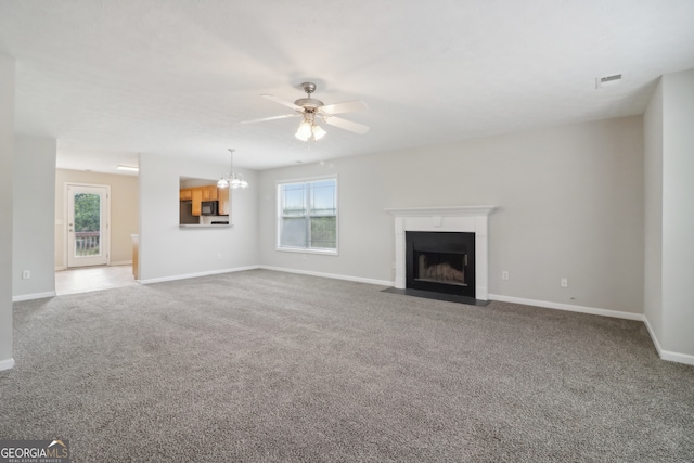 unfurnished living room featuring ceiling fan with notable chandelier, a healthy amount of sunlight, and carpet floors