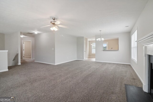 unfurnished living room with ceiling fan with notable chandelier, plenty of natural light, and carpet flooring