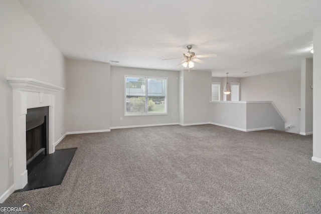 unfurnished living room with carpet flooring, a fireplace with flush hearth, a ceiling fan, and baseboards