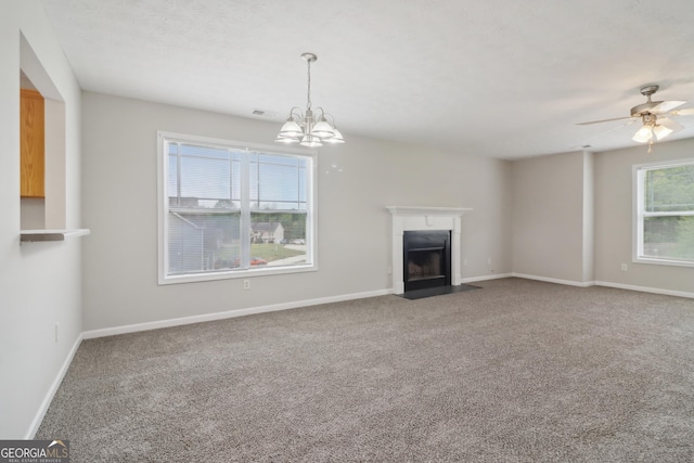 unfurnished living room with ceiling fan with notable chandelier, carpet flooring, a fireplace with flush hearth, visible vents, and baseboards