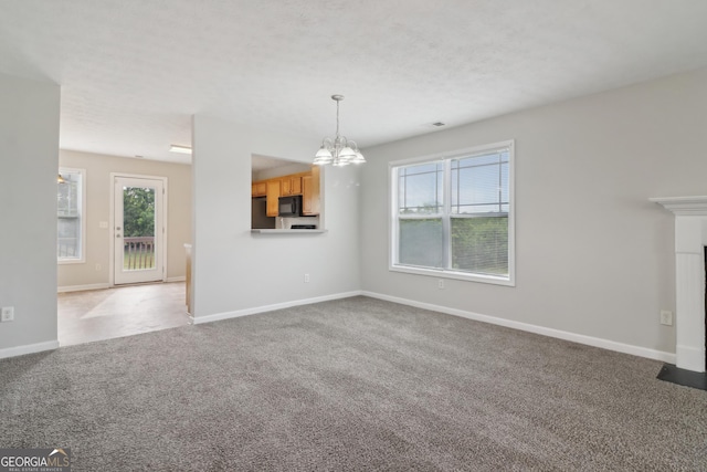 unfurnished living room with carpet, a textured ceiling, baseboards, and an inviting chandelier