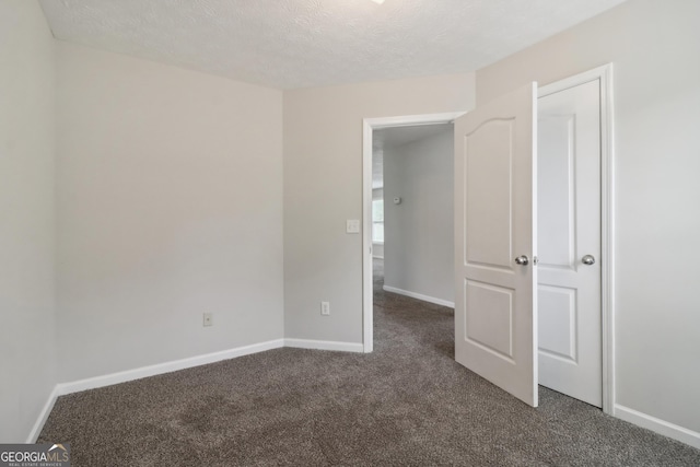 unfurnished bedroom featuring baseboards, dark carpet, and a textured ceiling