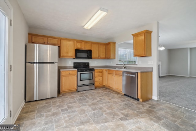 kitchen featuring stainless steel appliances, light colored carpet, light countertops, a sink, and baseboards