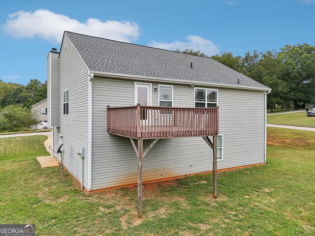 rear view of property featuring roof with shingles, a lawn, a chimney, and a wooden deck