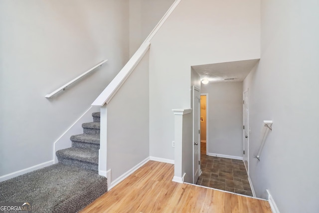 staircase with a towering ceiling, baseboards, and wood finished floors