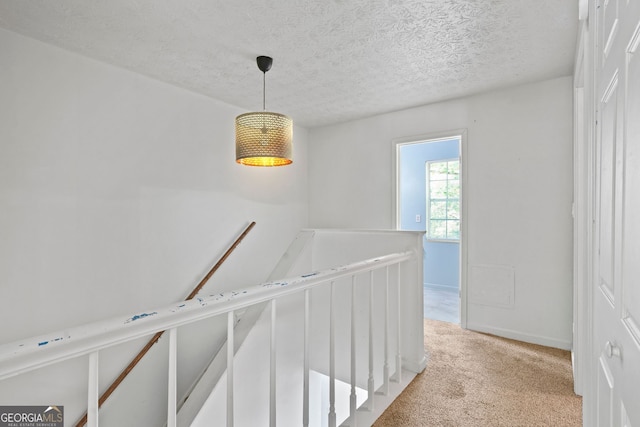 corridor with a textured ceiling and light carpet