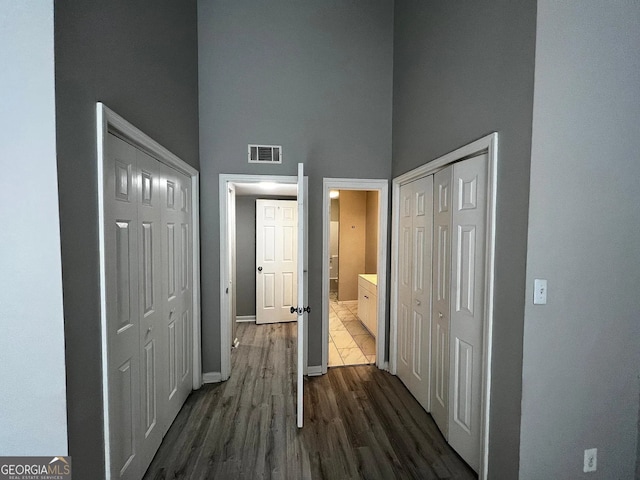 hallway featuring visible vents, baseboards, a high ceiling, and dark wood-style floors