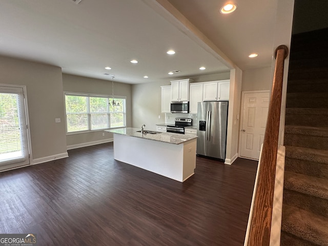 kitchen with white cabinets, light stone countertops, stainless steel appliances, dark hardwood / wood-style floors, and an island with sink