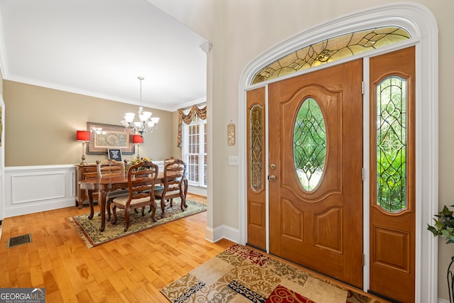 foyer entrance with ornamental molding, light hardwood / wood-style flooring, and an inviting chandelier