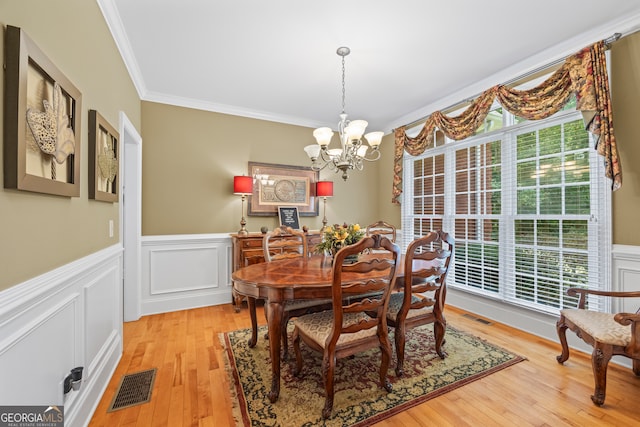 dining space with ornamental molding, an inviting chandelier, and light hardwood / wood-style floors