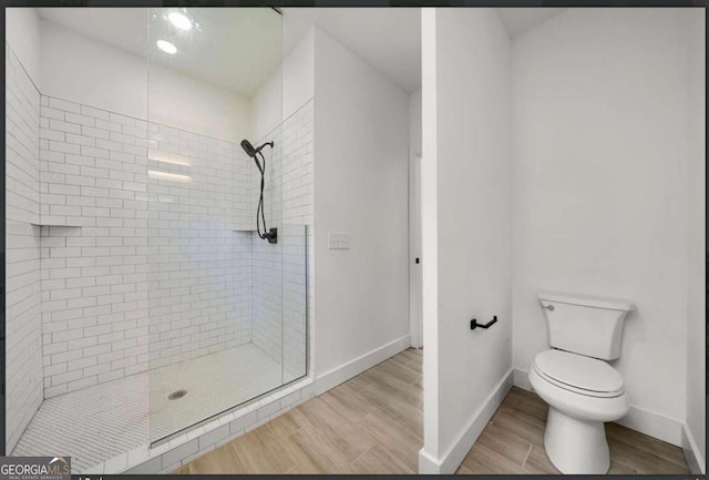 bathroom with toilet, wood-type flooring, and a shower with shower door