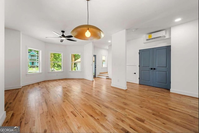 unfurnished living room with a wall mounted air conditioner, ceiling fan, and light hardwood / wood-style floors