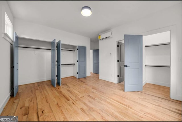 unfurnished bedroom with light wood-type flooring, two closets, and a wall mounted air conditioner