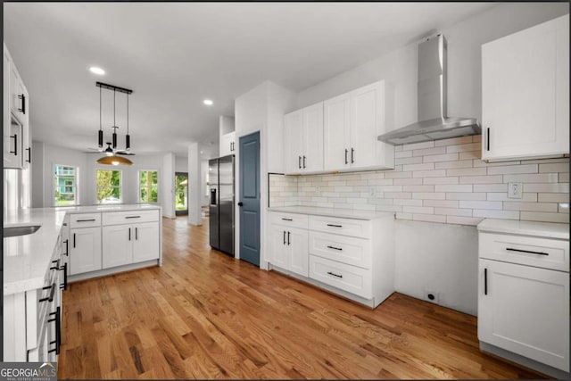 kitchen with light wood-type flooring, stainless steel fridge, wall chimney exhaust hood, and white cabinetry