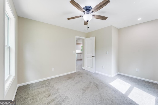 spare room with light colored carpet, a healthy amount of sunlight, and ceiling fan