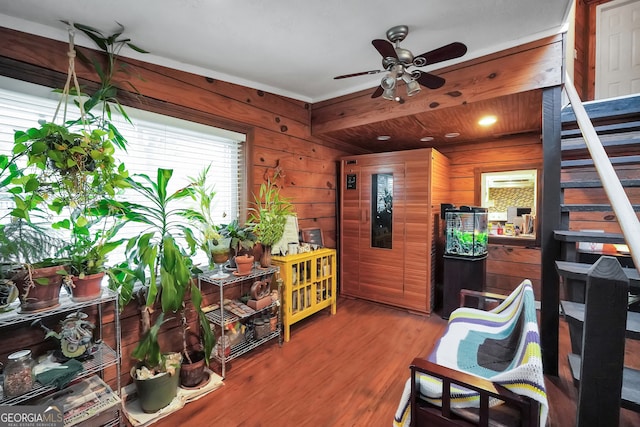 sitting room featuring wood-type flooring, ceiling fan, and wooden walls