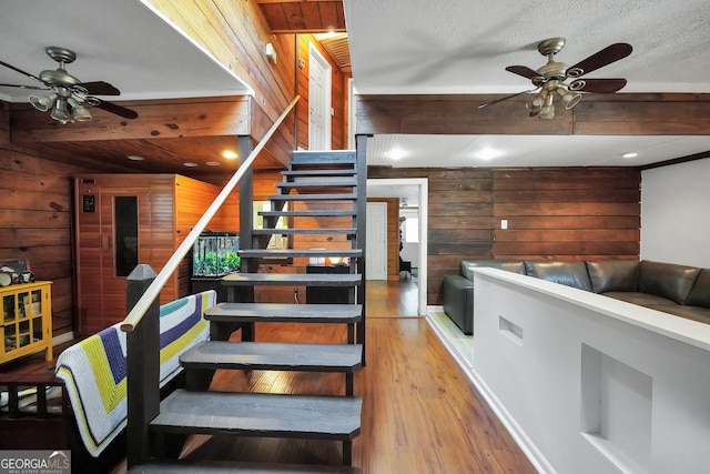 stairway with a textured ceiling, ceiling fan, wood-type flooring, and wooden walls