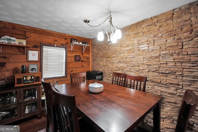 dining room with a notable chandelier, a textured ceiling, dark wood-type flooring, and wooden walls