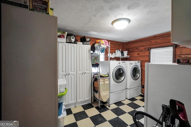 clothes washing area featuring a textured ceiling, cabinets, wood walls, and separate washer and dryer