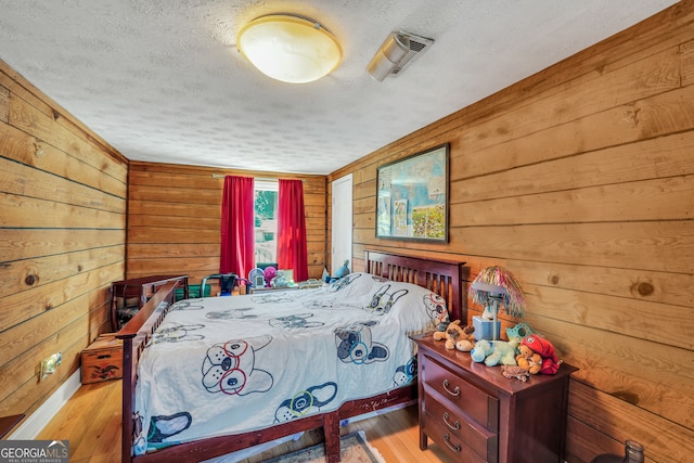 bedroom featuring a textured ceiling, light wood-type flooring, and wooden walls