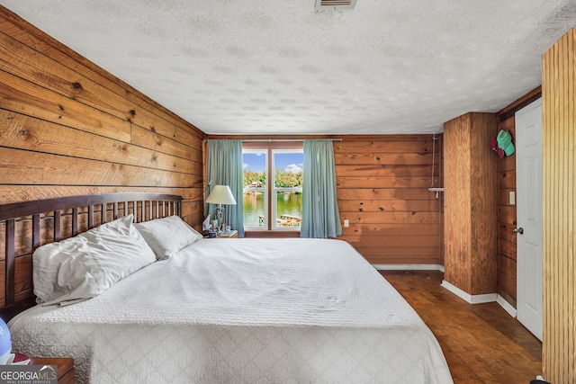 bedroom with a textured ceiling, wooden walls, and dark hardwood / wood-style floors