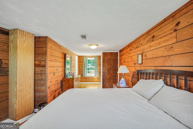 bedroom with ensuite bath, a textured ceiling, and wood walls