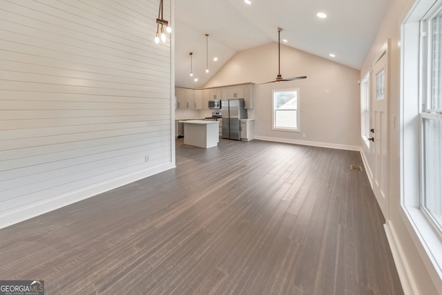 unfurnished living room featuring wood walls, high vaulted ceiling, dark hardwood / wood-style flooring, and ceiling fan