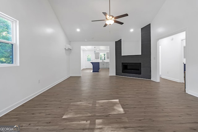 unfurnished living room with ceiling fan, a tiled fireplace, high vaulted ceiling, and dark hardwood / wood-style flooring