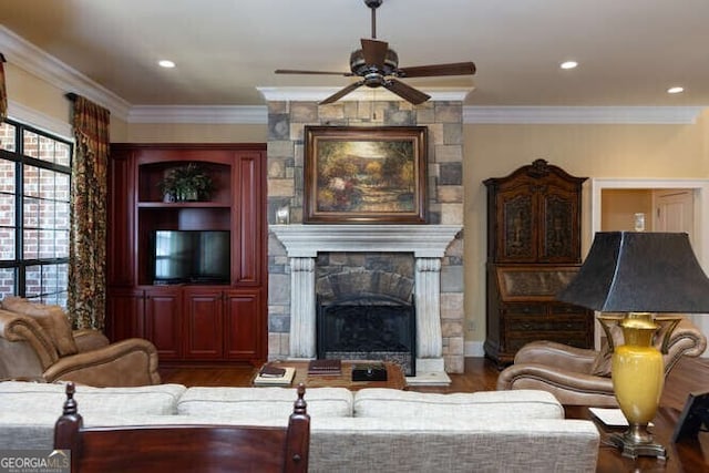 living room with ceiling fan, ornamental molding, a stone fireplace, and hardwood / wood-style flooring