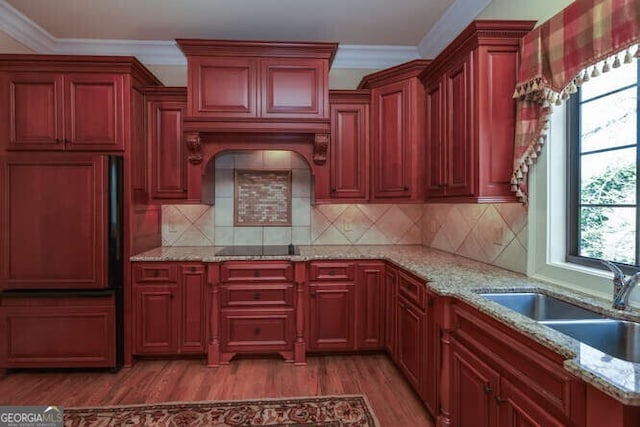 kitchen with light stone counters, paneled built in fridge, a sink, light wood-style floors, and crown molding