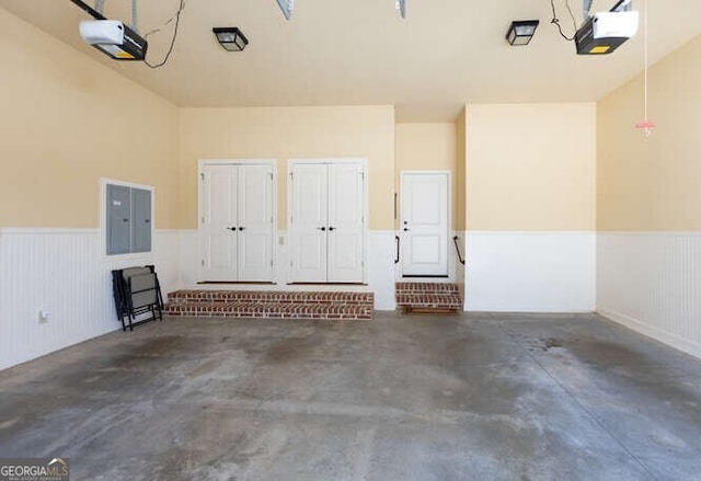 garage featuring electric panel, a garage door opener, and wainscoting