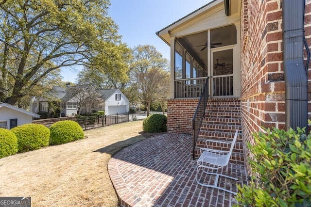 view of home's exterior with stairway, a ceiling fan, fence, a sunroom, and brick siding