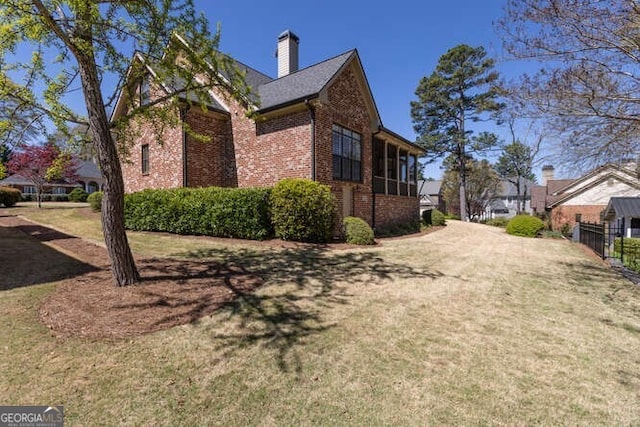 view of side of property with a yard, brick siding, and a chimney