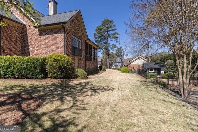 view of property exterior with brick siding, a lawn, a chimney, and fence