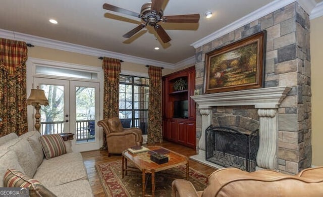 living room featuring a stone fireplace, french doors, ornamental molding, hardwood / wood-style flooring, and ceiling fan