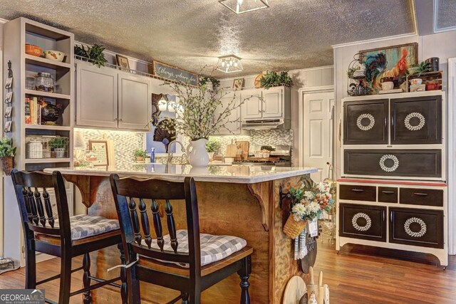 kitchen with stainless steel stove, dark hardwood / wood-style floors, kitchen peninsula, a breakfast bar area, and a textured ceiling