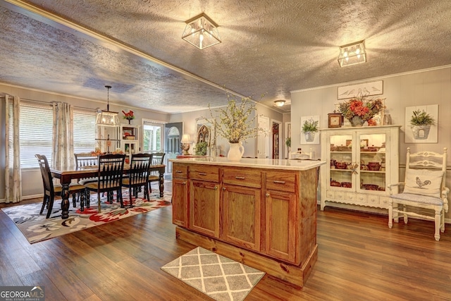 kitchen featuring a center island, crown molding, decorative light fixtures, dark wood-type flooring, and a textured ceiling