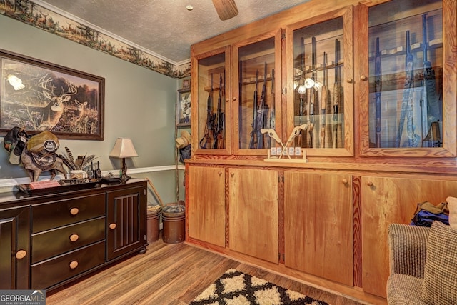 interior space with a textured ceiling, ceiling fan, ornamental molding, and light hardwood / wood-style floors