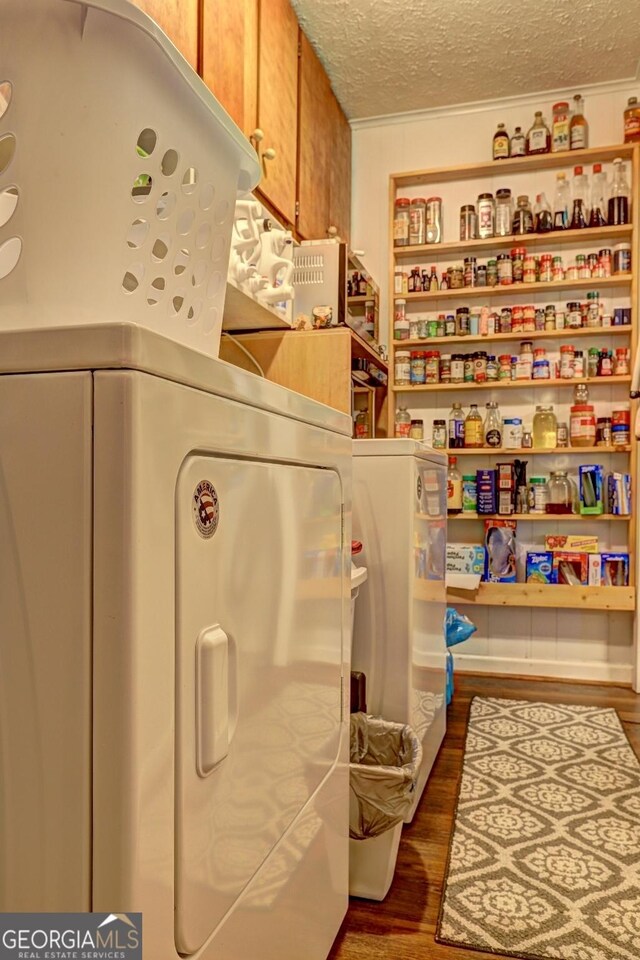 laundry room with a textured ceiling, dark wood-type flooring, washer and clothes dryer, and cabinets