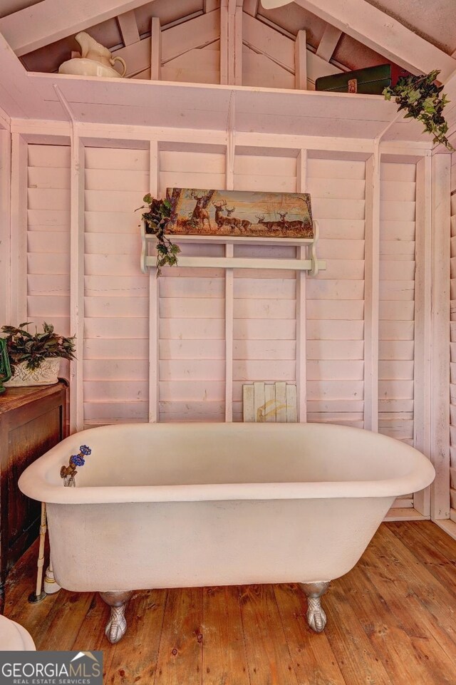 bathroom with wood-type flooring, a tub, and vaulted ceiling with beams