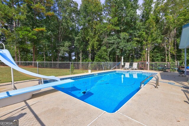 view of pool featuring a lawn, a water slide, a diving board, and a patio area